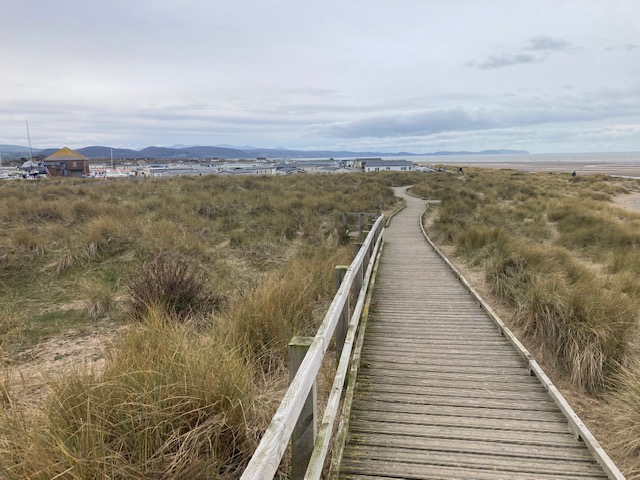 A boardwalk through the sand dunes, with caravans, boats and the hills beyond
